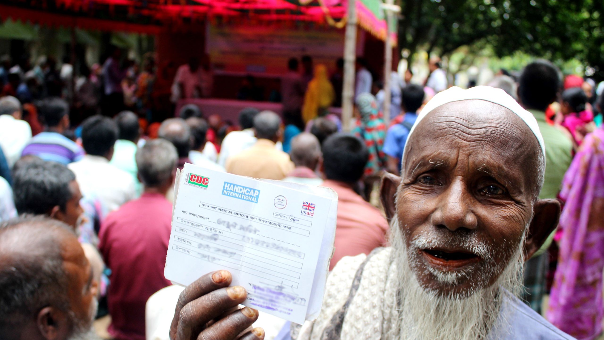 A man is seen holding up his cash voucher after his home was destroyed during floods in Bangladesh. Image by Sharaful Hossain, Humanity & Inclusion, alert B003 Bangladesh.